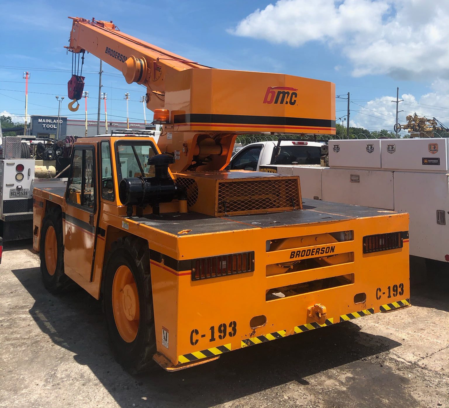Orange heavy-duty crane vehicle parked on a concrete surface under a blue sky.