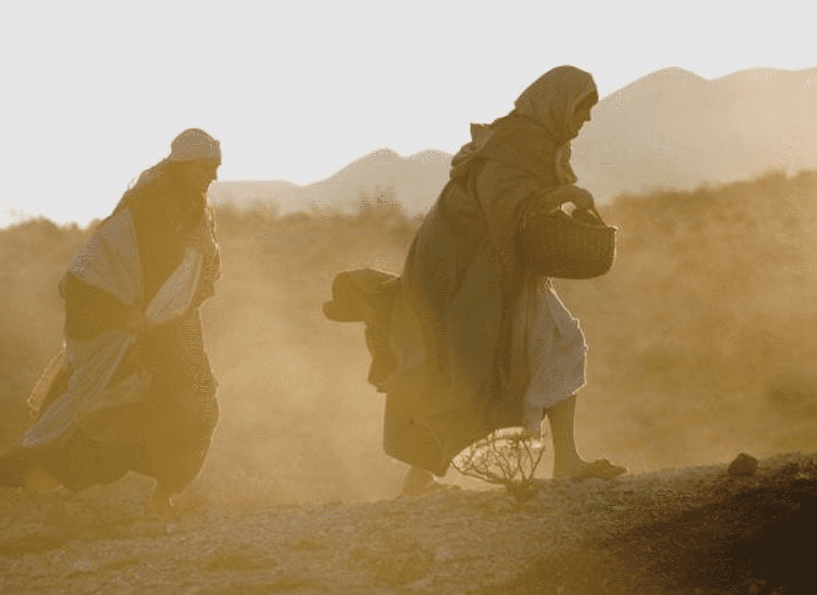 Two people walking in a dusty landscape.